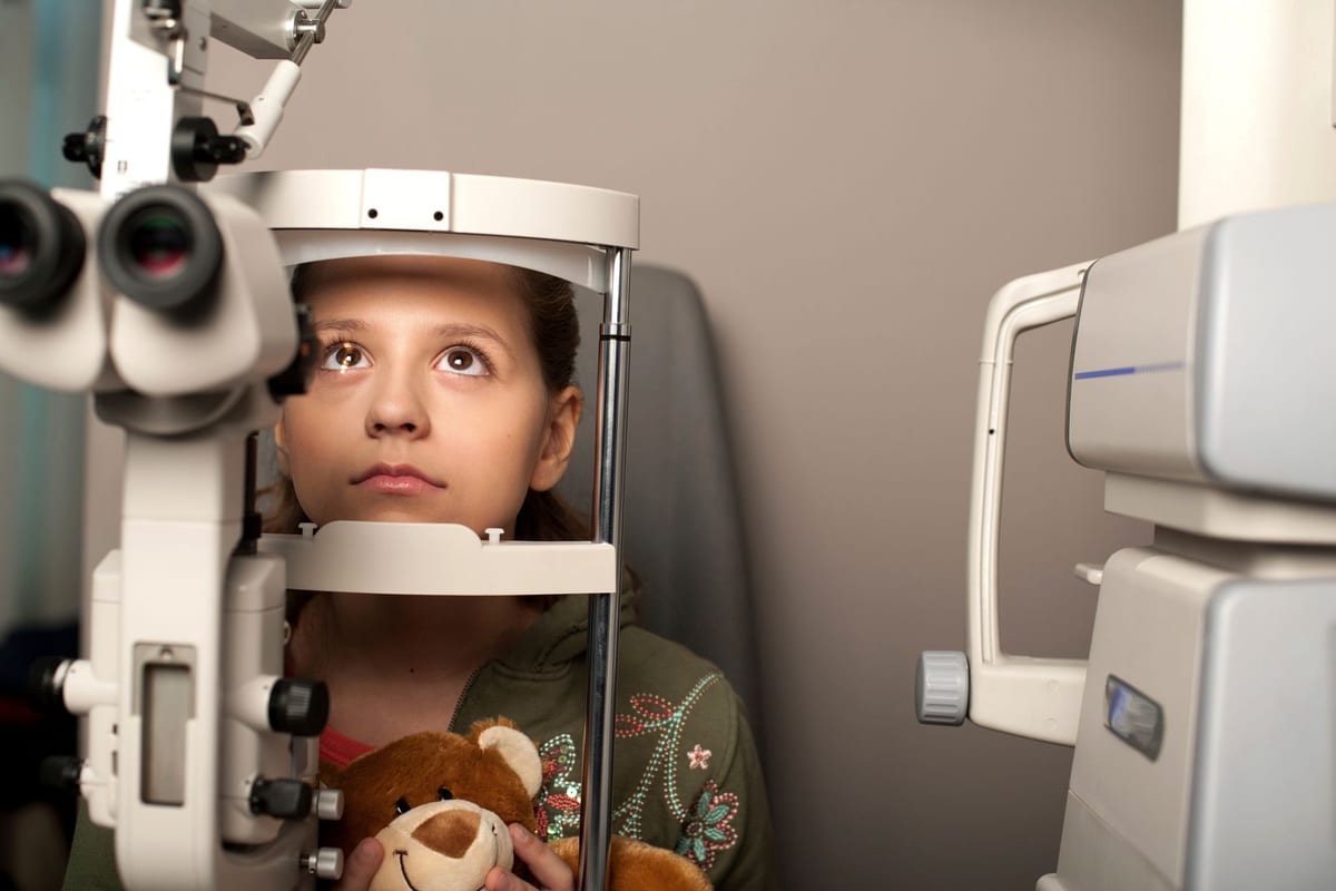 A girl holding a teddy bear at the slit lamp during her eye exam
